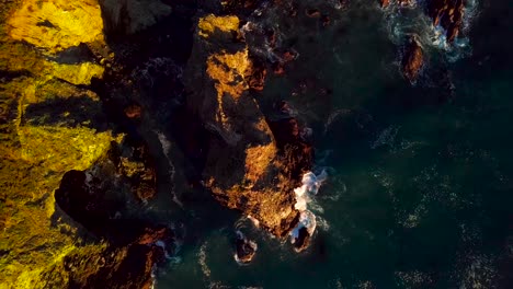 The-last-sunlight-of-day-illuminates-a-blue-ocean-wave-crashing-into-rocky-cliffs-in-Big-Sur-California