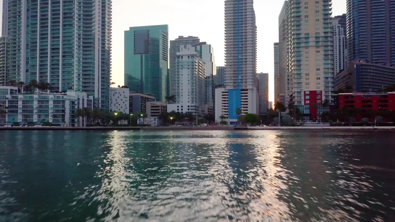 Aerial view low over the sea towards high rise buildings, in the Brickell district, during sunrise, in Miami, Florida, USA - tilt up, drone shot