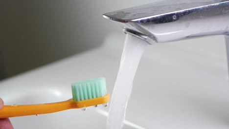 close-up of a toothbrush being rinsed under running water in a sink