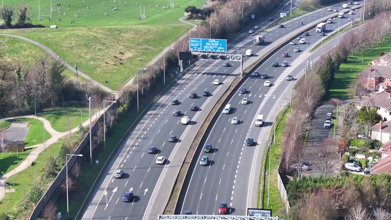 Trafik i sydgående retning på M50 motorvejen og Dublins forstadslandskab i klart solrigt vejr, Irland.