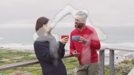 Animation-of-house-shape-over-diverse-couple-drinking-coffee-on-balcony