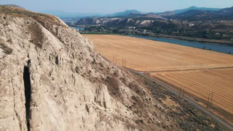 beautiful aerial view of rocky hill next to a road and field with lake and mountains in the distance