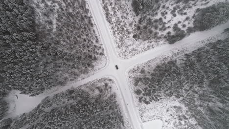 aerial top down of car on snowy rural junction surrounded by snow-covered forest trees in nature - orbiting shot