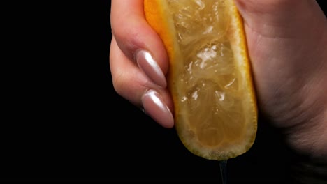 static slow motion shot of yellow ripe lemon squeeze with leaking juice held by a beautiful manicured woman's hand against a black background