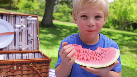 a boy looks at the camera while biting a watermelon before swallowing and smiling