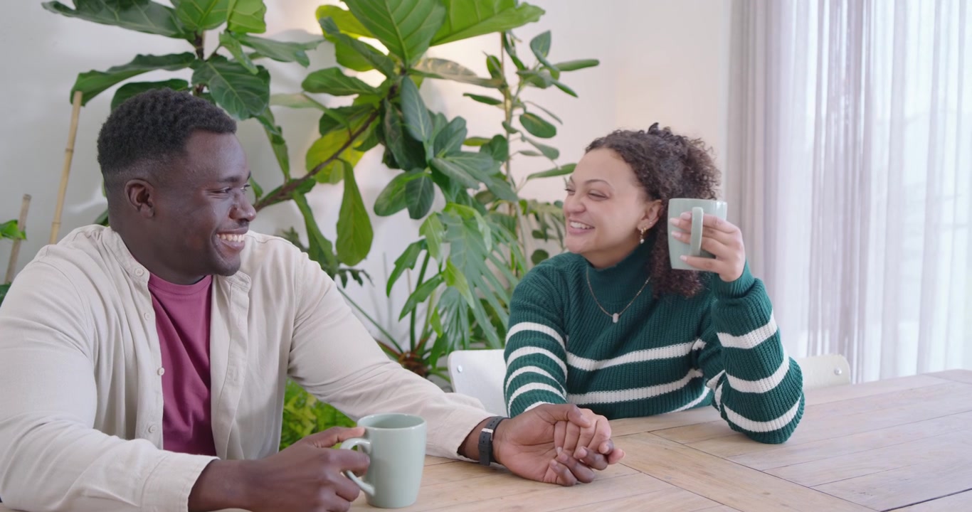African American couple talking at dining table woman touching arm man clinking green mugs bonding
