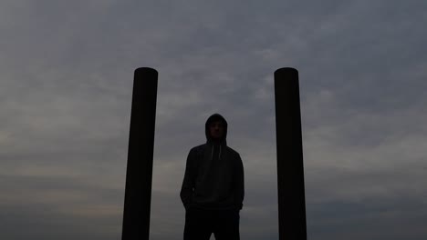 young caucasian man wearing hoodie stands between two pillars while staring into the distance. push in slider movement