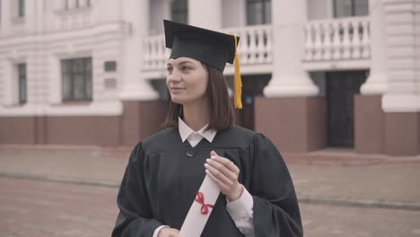 Linda-Estudiante-De-Posgrado-En-Bata-Y-Gorra-Con-Diploma-Mirando-A-La-Cámara-Y-Sonriendo-1