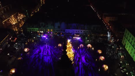 Revealing-Christmas-tree-of-Kaunas,-City-Hall-tower-in-foreground