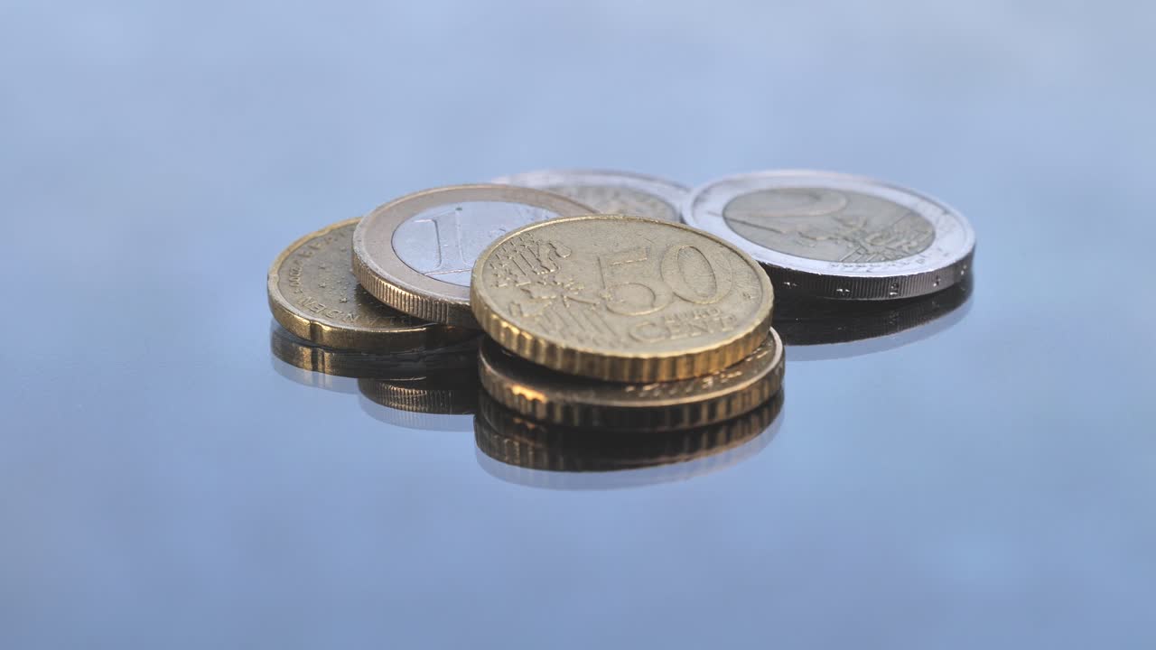 A man's hand carefully places various euro coins onto a glossy, reflective surface
