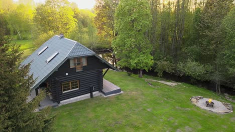 log cabin by the river during a sunny winter evening with green yard and fireplace in the backyard