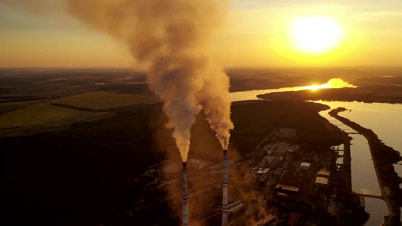 Two pipes with thick smoke. Industrial factory surrounded by nature in the evening. Air pollution. Aerial view. Slow motion camera.