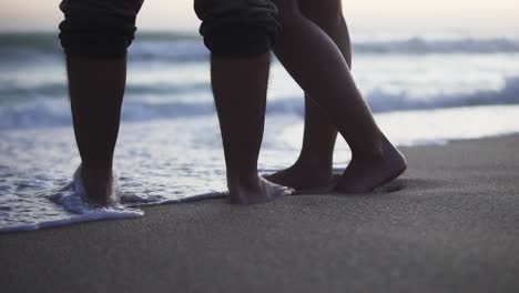 static slow motion shot of a couple in love standing in the sand on the beach with calm waves from the sea during a romantic sunset