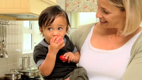 mother in kitchen holding baby with red apple