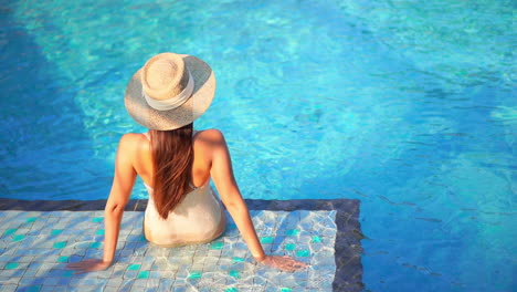 Detrás-De-Una-Mujer-Atractiva-Sentada-En-El-Borde-De-La-Piscina-Azul-En-Un-Día-Soleado-De-Verano,-Marco-Completo