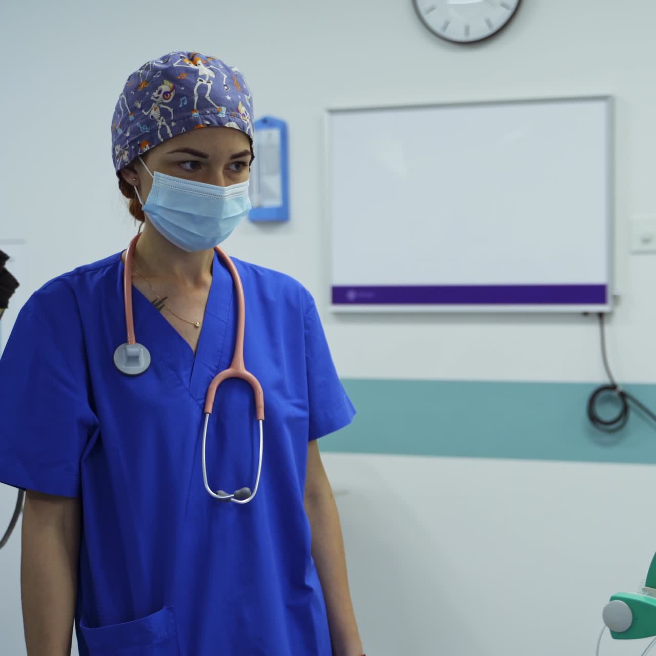 Young female doctor anesthesiologist with stethoscope hanging on her shoulders. Medic turns the handle on the equipment in surgery room