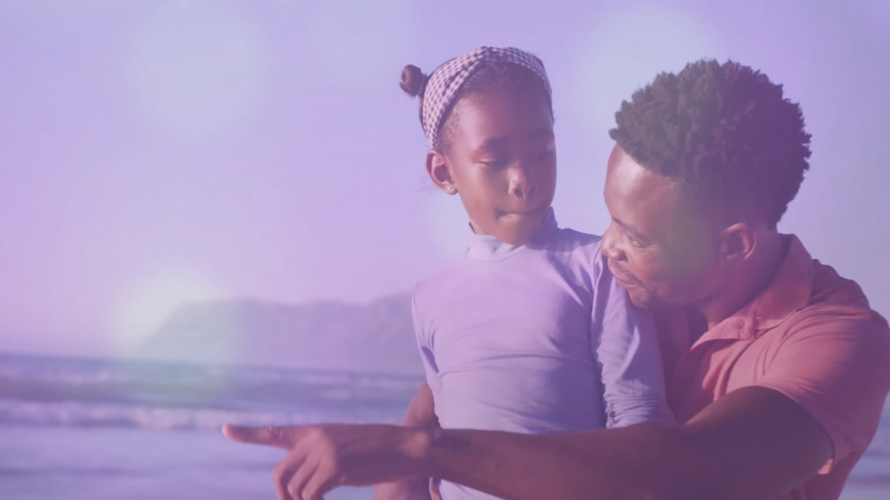Lifestyle father speaking softly holding daughter wearing headband pointing toward island at beach
