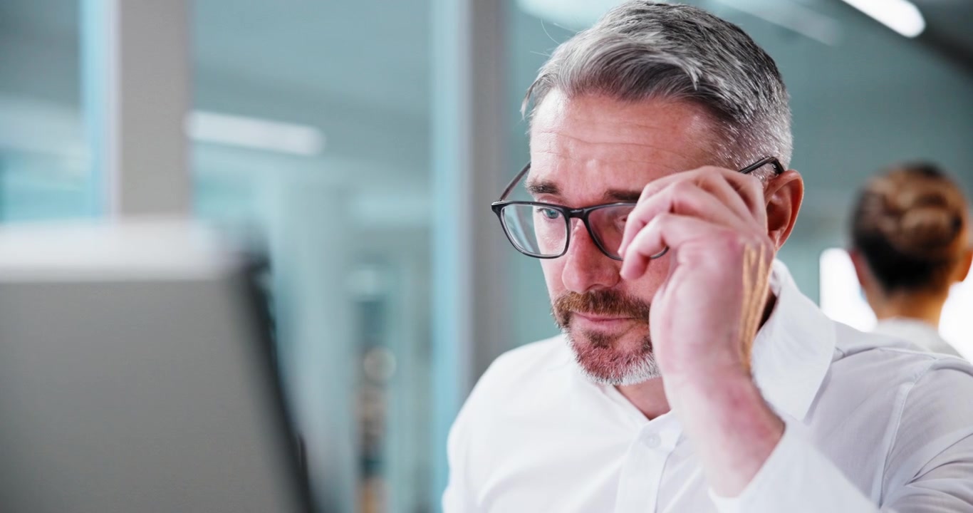 Uomo d'affari stressato che si stropiccia gli occhi e indossa gli occhiali in ufficio