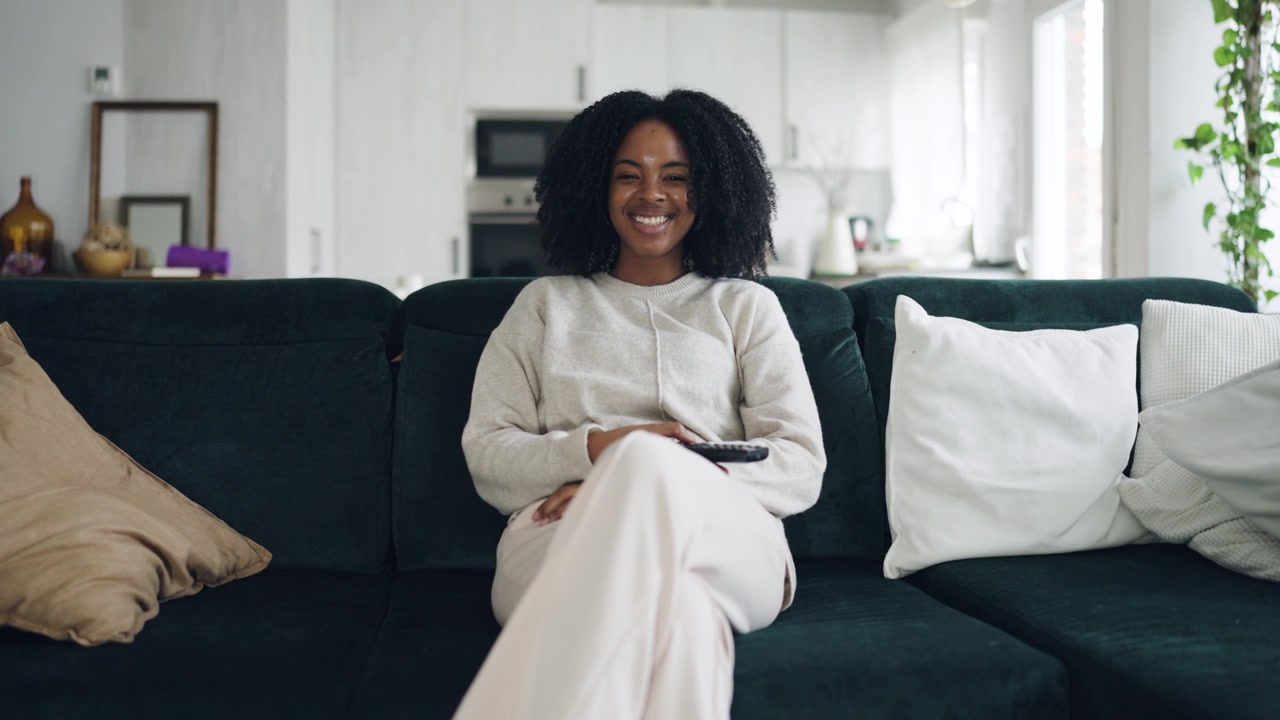 Glad afroamerikansk kvinde ser tv og smiler på sofaen