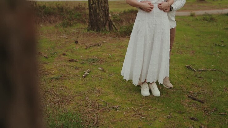 Couple standing together on grass in forest clearing while embracing