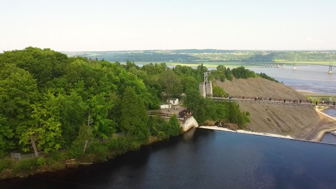Aerial View of a Suspension Bridge over a River with a Waterfall and Lush Forest