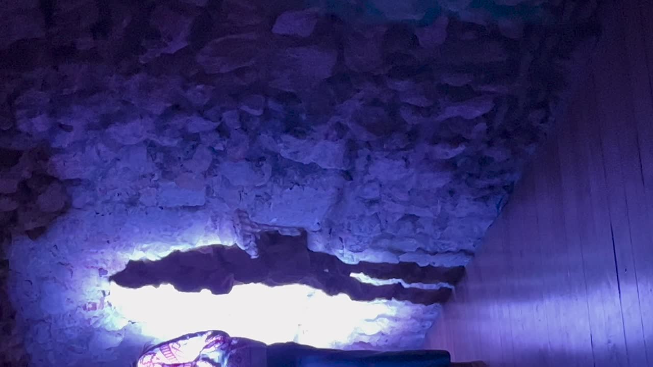 Vertical video of a person standing in bright light, casting a dramatic shadow on a rugged stone wall. The textured relief and play of light and shadow create a striking visual effect.