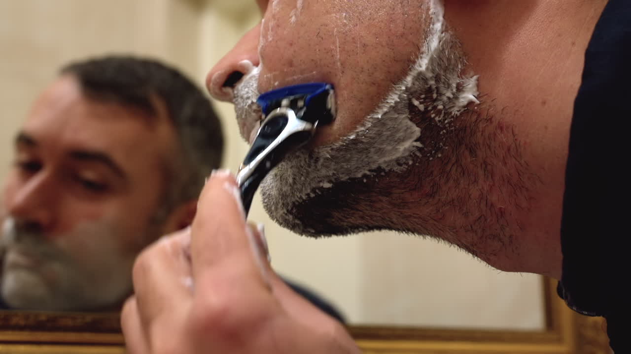 Close de um homem se barbeando em frente ao espelho no banheiro