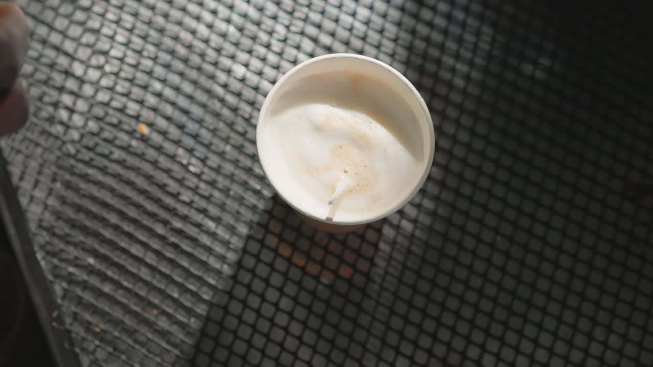 Close-up of a person's hand carefully adjusting a coffee cup, likely preparing a drink with foam art or decoration. The image captures the intimate process of crafting a coffee beverage