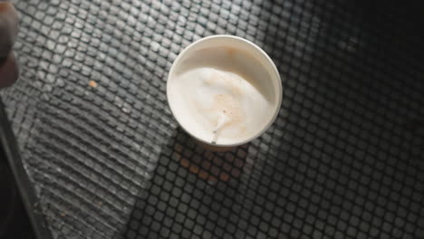 close-up of a person's hand carefully adjusting a coffee cup, likely preparing a drink with foam art or decoration. the image captures the intimate process of crafting a coffee beverage