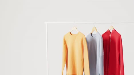 video of close up of yellow, blue and red sweaters hanging on clothes rail on white background