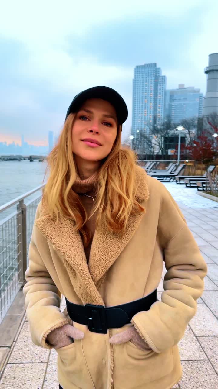 Ritratto di donna vicino allo skyline di Manhattan sull'East River. Ritratto di profilo di donna con cappotto beige e berretto nero vicino all'East River con lo skyline di Manhattan sullo sfondo.