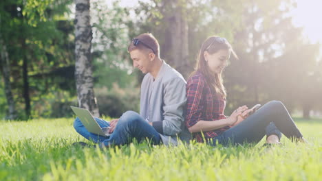 Students-Studying-In-The-Park---Use-A-Laptop-And-A-Smartphone-They-Sit-On-The-Green-Grass-Hd-Video