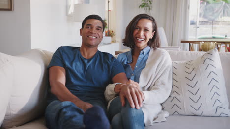 Young-adult-African-American-couple-sitting-in-their-living-room-watching-TV-together--laughing,-close-up