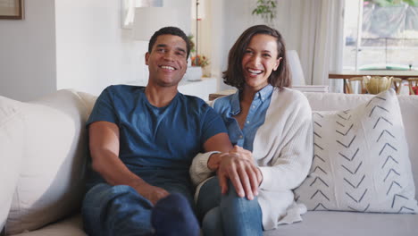 young adult african american couple sitting in their living room watching tv together  laughing, close up