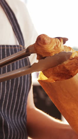 waitress packing croissants in paper bag at cafã©