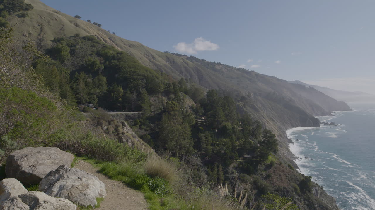 Rekaman panning dari sisi gunung menuju Samudra Pasifik di pantai Big Sur California dengan ombak menghantam pantai berbatu