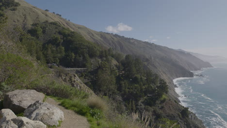 Schwenk-Von-Der-Bergseite-Zum-Pazifischen-Ozean-Am-Strand-Von-Big-Sur-California-Mit-Wellen,-Die-An-Einer-Felsigen-Küste-Krachen