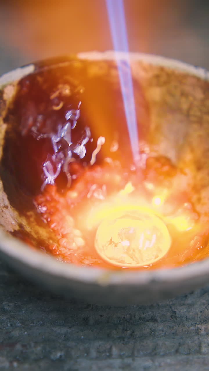 CU: bright orange drop of molten gold heats in special fireproof cup on asbestos sheet in craft jewelry shop extreme close