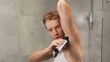 attractive young athletic man shaves armpits with electric cordless razor