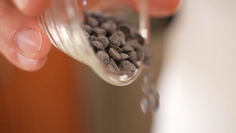 pouring chocolate chips from plastic cup, close up in slow motion with copy space