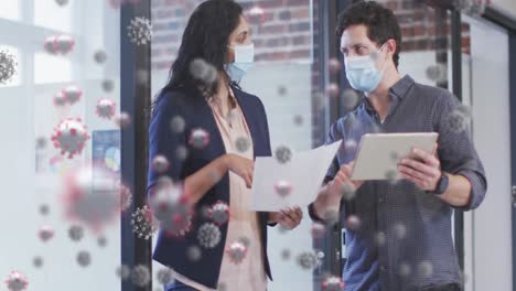 Animation-of-covid-19-cells-over-colleagues-in-face-masks-with-digital-tablet-in-office