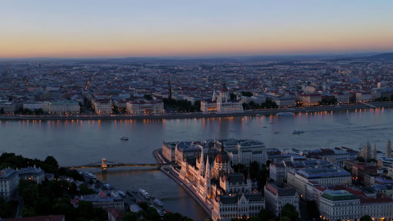 Aerial video view of a cityscape at dusk, showcasing illuminated buildings along a river