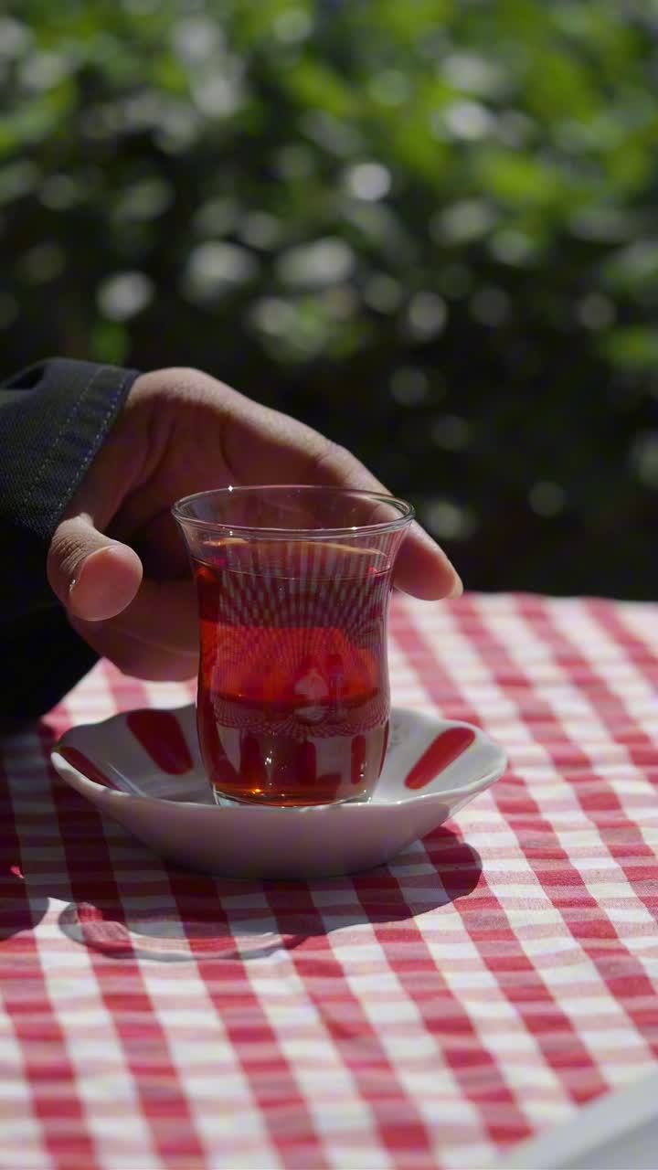 Kırmızı Kareli Bir Masa Örtüsü Üzerindeki Bir Bardak Çayı Kaldıran El.