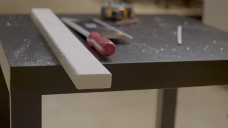 Static-shot-of-a-worker-measuring-and-marking-a-plank-of-wood-ready-to-be-cut-in-a-workshop