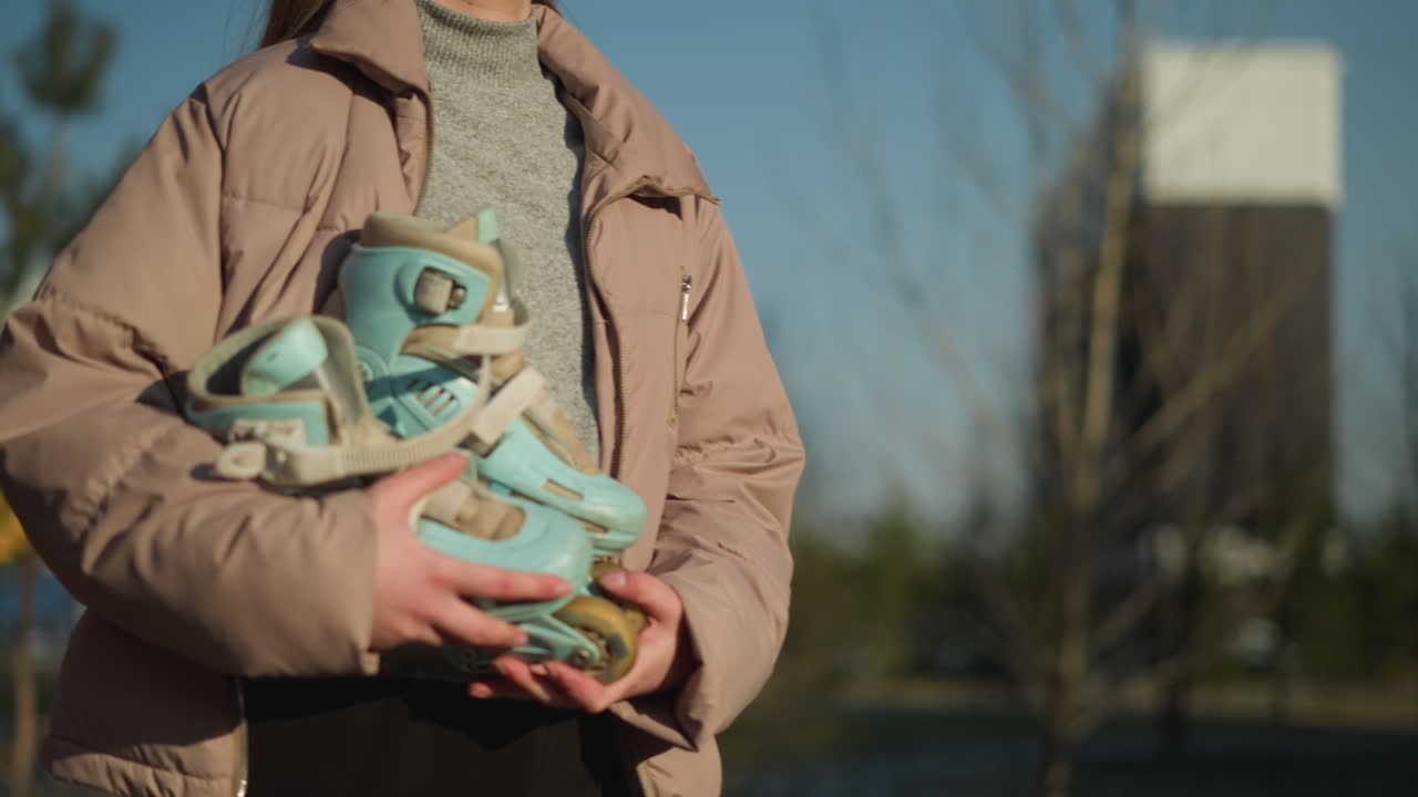 두 손으로 스케이트보드를 들고 은 날에 걸어가는 소녀. 그녀는 은 야외 환경을 걸어다니면서 앞을 바라보며 복아 재과 회색 내부 셔츠를 입고 있습니다.