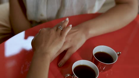 Two-unrecognizable-womans-caressing-hands-while-having-coffe