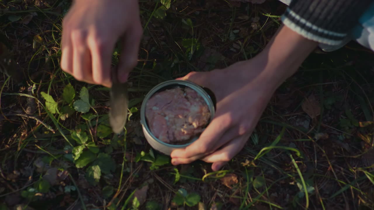 top down view person seated opening can food cover outdoors camping nature forest adventure survival meal preparation picnic cooking hands travel wilderness leisure young lifestyle environment