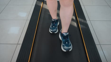 close up leg view of person in canvas sneakers walking on treadmill, focus on movement and stride, tiled gym floor beneath, fitness concept with dynamic motion and workout atmosphere