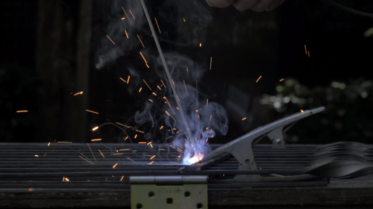 Man welding together a fence outdoors with a big flame from the welder and lots of smoke and flashes with copy space