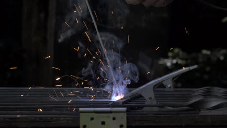 man welding together a fence outdoors with a big flame from the welder and lots of smoke and flashes with copy space